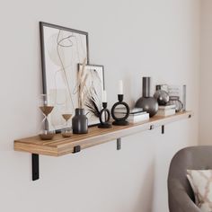 a shelf with vases, candles and pictures on it next to a gray chair