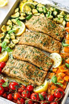 salmon, zucchini, and tomatoes in a pan with lemons on the side