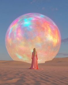 a woman standing in front of a giant bubble ball on top of a sandy field