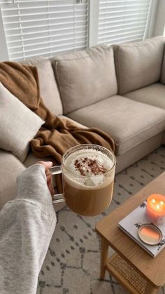 a person holding up a cup of coffee in front of a couch with candles on it