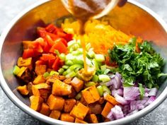 a bowl filled with chopped vegetables and dressing being drizzled over the top