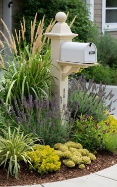 a white mailbox sitting in the middle of a flower bed next to a house