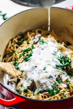 a red pot filled with pasta covered in white sauce and parmesan cheese being poured into it