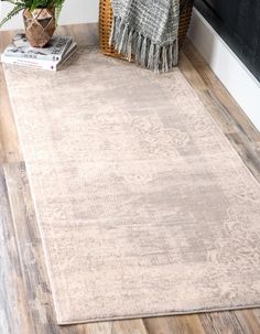 a beige rug on a wooden floor next to a plant