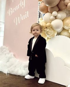 a little boy standing in front of a wall with balloons on it's side