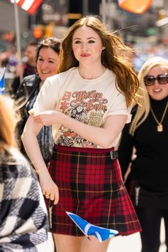 a woman in a plaid skirt is walking down the street with her hands on her hips