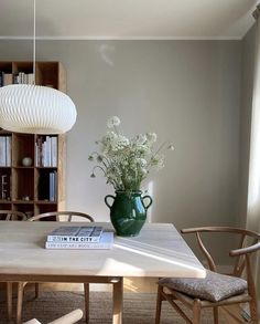 a green vase sitting on top of a wooden table next to a book shelf filled with books