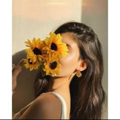 a woman with sunflowers in her hair is looking at the camera while she's holding it up to her face