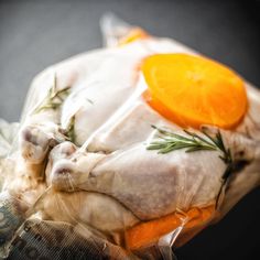 a chicken wrapped in plastic with carrots and rosemary