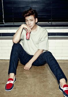 a young man sitting on the ground drinking from a pink water bottle with his legs crossed