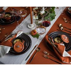 the table is set with black and orange plates, silverware, and wine glasses