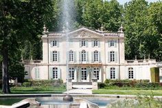 a large white house with a fountain in front of it and trees surrounding the building