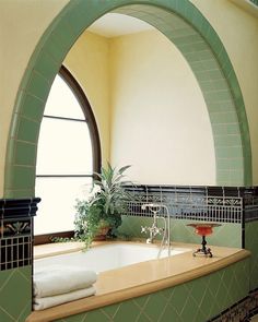 a bathroom with green tile and an arched window above the bathtub is pictured in this image