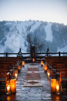 candles are lit in front of rows of wooden chairs on a deck overlooking a snowy mountain