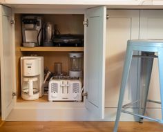 an open cabinet in a kitchen filled with appliances and coffee maker on top of a wooden floor