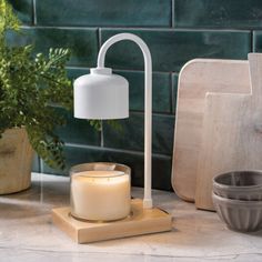 a white candle sitting on top of a wooden block next to a potted plant