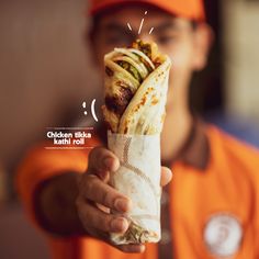 a man in an orange shirt is holding a burrito