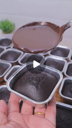 a person is holding a spoon over some chocolate pudding in tins with other trays behind them