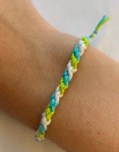 a person wearing a colorful bracelet on their arm with a yellow and blue string attached to it