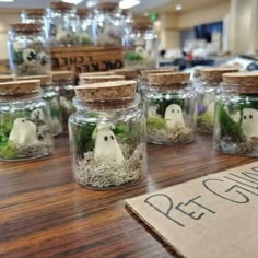 several glass jars filled with plants and fake ghost heads on a table in a store