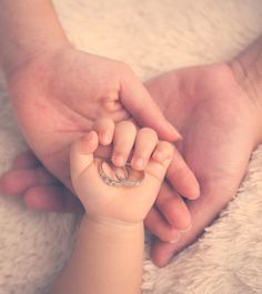 a close up of a person holding a baby's hand with a ring on it