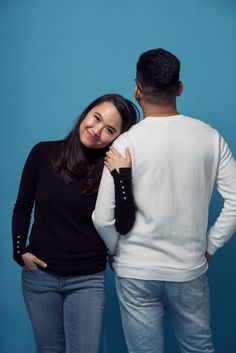 a man and woman standing next to each other in front of a blue wall smiling