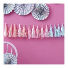 paper fans and tassels hanging on a pink wall next to a white chair