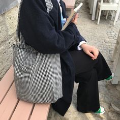 a woman sitting on a bench reading a book while wearing black and white checkered coat