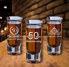 three shot glasses sitting on top of a wooden table with the 50th anniversary logo printed on them