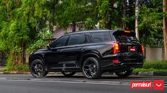 the rear end of a black suv parked in front of a tree lined street with lots of green trees