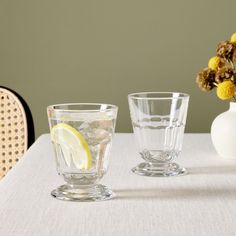 two glasses on a table with flowers in the vase and one glass filled with water