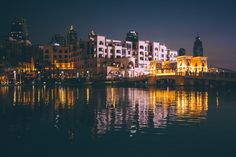 a bridge that is over some water with buildings in the background and lights on it