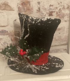 a black top hat with holly and berries on it sitting on a white table next to a brick wall