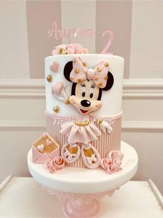 a minnie mouse birthday cake with pink decorations and gold trimmings on a white pedestal