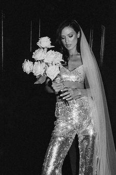 black and white photograph of a woman in sequin pants holding flowers with long veil