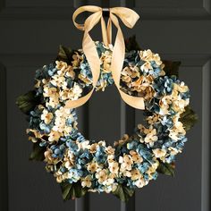 a wreath with blue and white flowers hanging from the front door on a black door