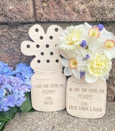 two mason jars with flowers in them sitting next to each other on the ground near a stone wall