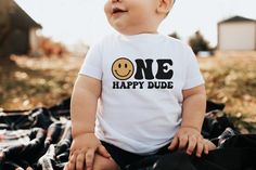 a baby sitting on top of a blanket wearing a one happy dude t - shirt