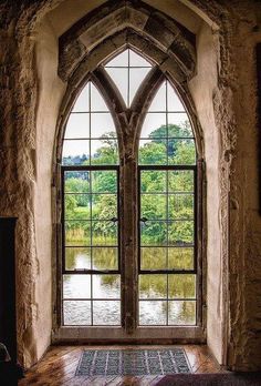 an arched window in a stone building with a lake below it and trees outside the window