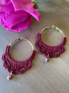 two pairs of earrings sitting on top of a wooden table next to a pink flower