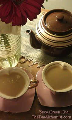 two cups of coffee sit next to each other on a table with a flower in a vase