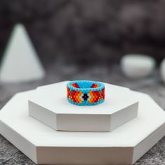 Celebrate vibrant boho style with this colorful tribal-style beaded ring, expertly handcrafted from high-quality Delica beads. This ring features a stunning gradient transitioning from white, yellow, orange, and red to copper, complemented by a light blue trim. The intricate tribal style inspired pattern and bold colors make it a unique and eye-catching accessory, perfect for adding a touch of color to any outfit. Ideal for those who appreciate unique, artisan jewelry, this ring is perfect for e Bohemian Multicolor Rings For Festival, Blue Bohemian Rings For The Beach, Blue Bohemian Rings For Beach, Bohemian Blue Rings For Beach, Bohemian Multicolor Rings For Jewelry Making, Bohemian Multicolor Rings For Gifts, Multicolor Bohemian Rings For Gifts, Bohemian Multicolor Rings As Gift, Adjustable Bohemian Ring For Festivals