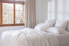 a bed with white sheets and pillows in front of a window