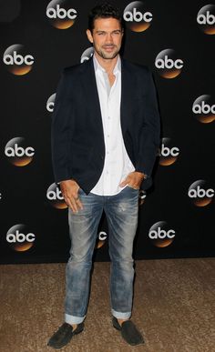 a man standing in front of a black wall wearing jeans and a blazer jacket