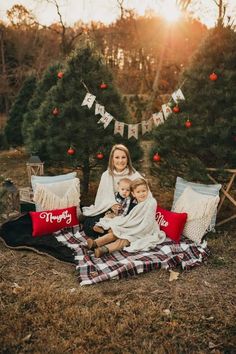 a woman and two children sitting on a blanket in front of a christmas tree at sunset