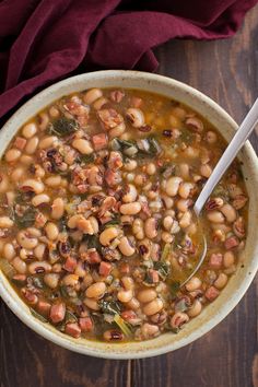 a white bowl filled with beans and greens on top of a wooden table next to a red cloth