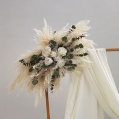 an arrangement of flowers and feathers is displayed on the back of a white chair with drapes