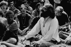 a group of people sitting on the ground in front of a man with long hair