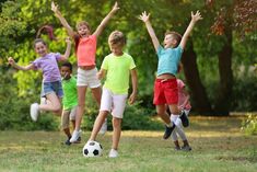 several children are playing with a soccer ball on the grass in front of some trees