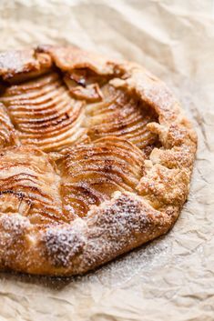 an apple pie with powdered sugar on top sits on wax paper and is ready to be eaten